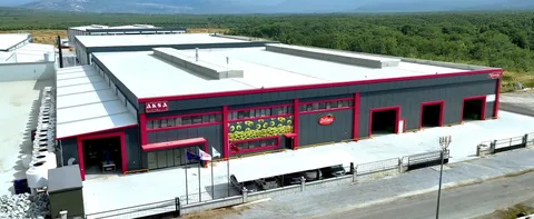 Aksa Zeytincilik'in Akhisar Süleymanlı OSB'deki üretim tesisinin havadan görünümü: antrasit cepheli, kırmızı şeritli fabrika binası; cephede AKSA Zeytincilik, Zeliva ve Yörem tabelaları; arkada zeytinlikler (firma görseli)